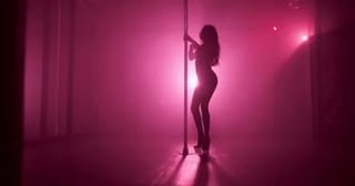 Silhouette of a pole dancer performing against vibrant pink and magenta stage lighting