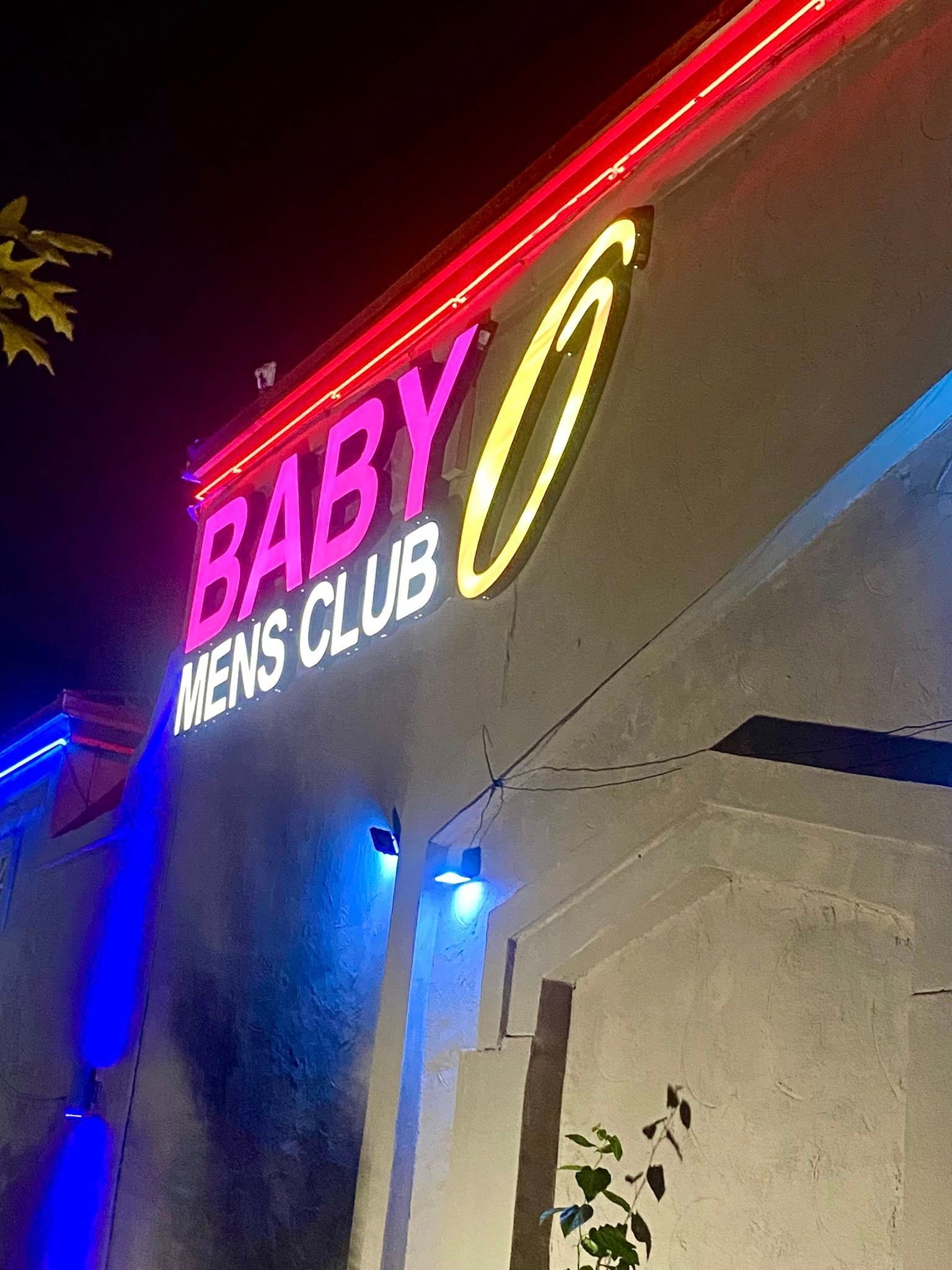 Neon sign for Baby Mens Club with red, magenta, and yellow glowing lights on building facade at night